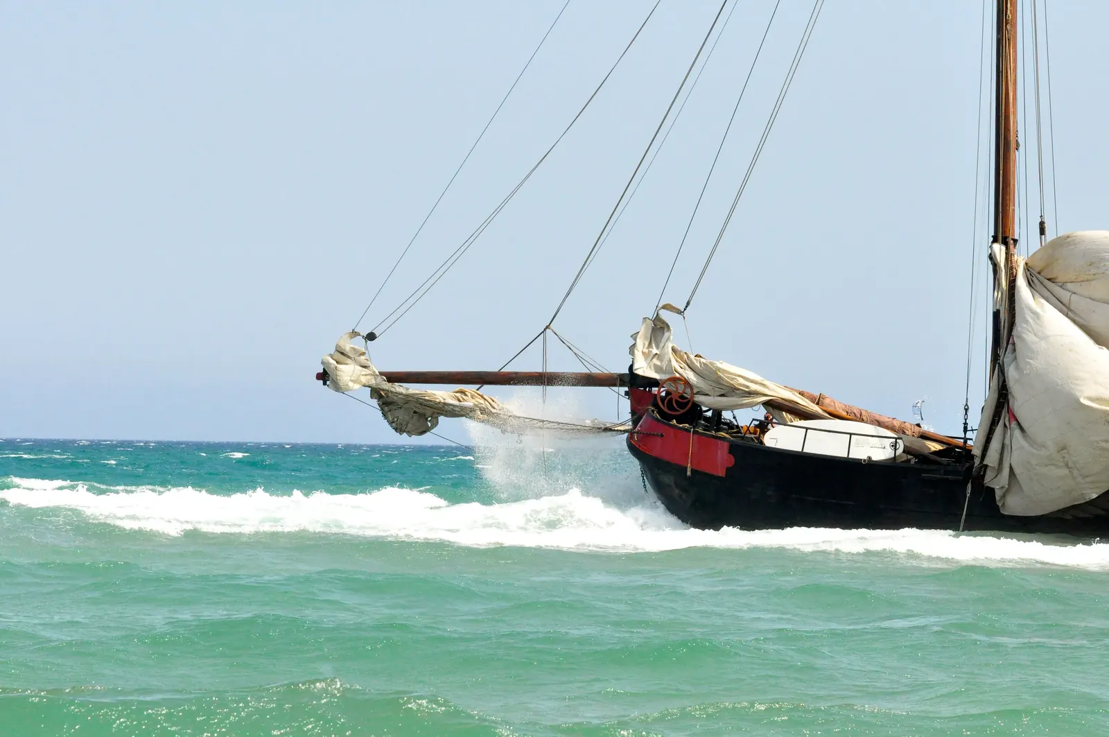 Vieux voilier à coque noire et liston rouge, l'étrave dans la vague